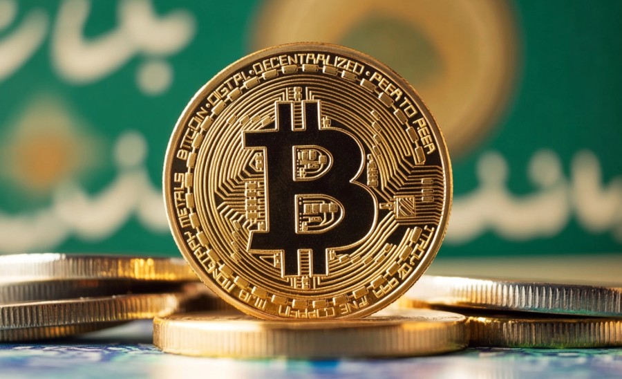 イランの国旗を背景に置かれたビットコインの物理コイン。中東情勢と仮想通貨市場の関係を象徴